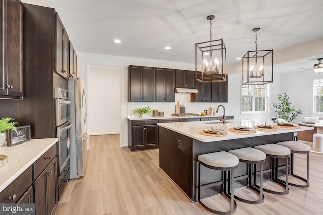 kitchen with stainless steel appliances, light wood-type flooring, sink, a breakfast bar, and a kitchen island with sink