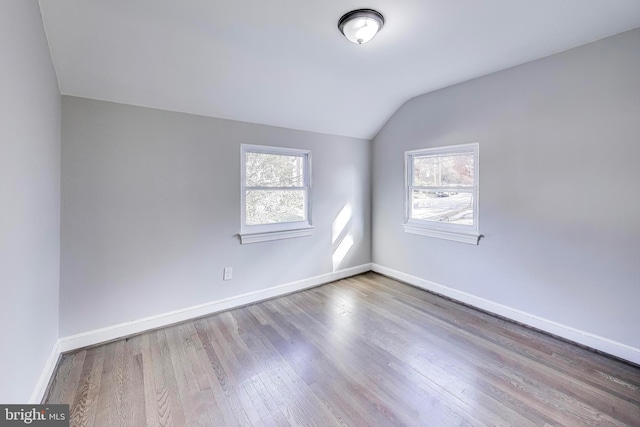 unfurnished room featuring a wealth of natural light, lofted ceiling, and hardwood / wood-style flooring