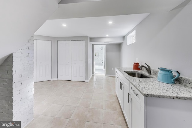 kitchen featuring white cabinets, light tile patterned floors, sink, and light stone countertops