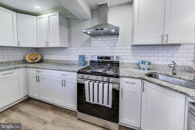 kitchen with decorative backsplash, sink, stainless steel gas stove, wall chimney range hood, and white cabinetry