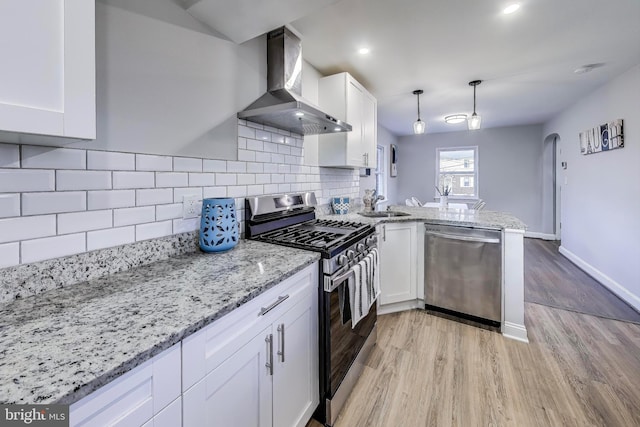 kitchen featuring stainless steel appliances, light wood-type flooring, white cabinets, wall chimney range hood, and pendant lighting