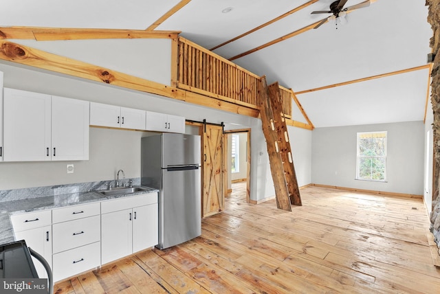 kitchen with stainless steel refrigerator, sink, a barn door, vaulted ceiling, and light wood-type flooring