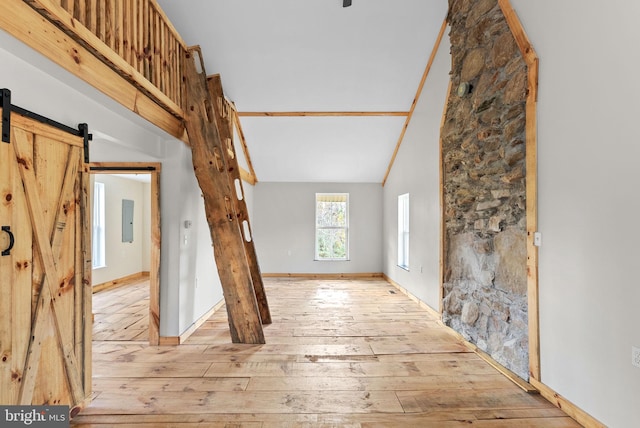 interior space with a barn door, light hardwood / wood-style flooring, lofted ceiling, and electric panel