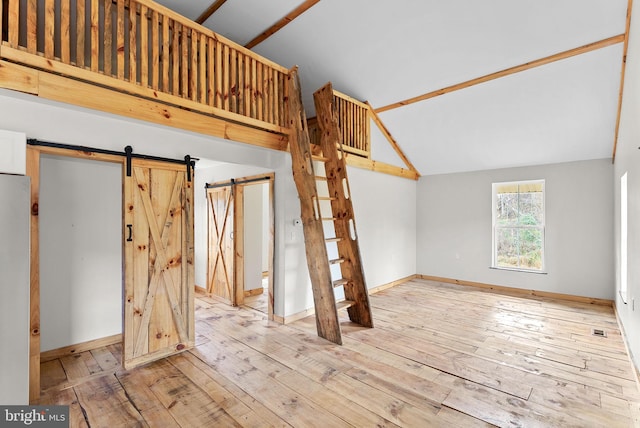 unfurnished living room featuring light wood-type flooring, vaulted ceiling, and a barn door