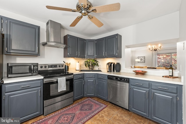 kitchen featuring tile patterned floors, wall chimney exhaust hood, ceiling fan with notable chandelier, stainless steel appliances, and gray cabinets