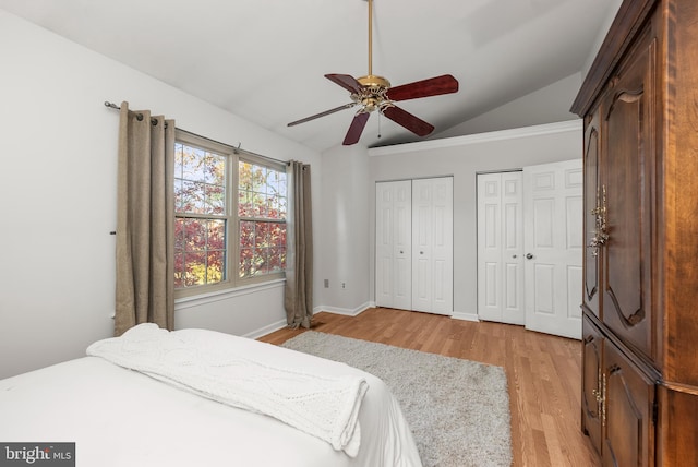 bedroom featuring ceiling fan, light hardwood / wood-style floors, lofted ceiling, and two closets