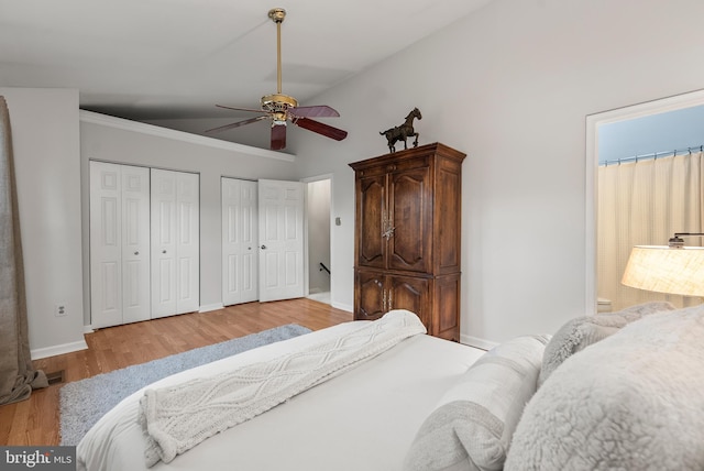 bedroom with ceiling fan, two closets, high vaulted ceiling, and light hardwood / wood-style flooring