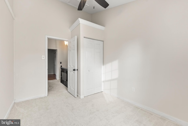 unfurnished bedroom featuring ceiling fan, light colored carpet, a towering ceiling, and a closet