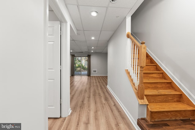 hallway with light wood-type flooring and a drop ceiling