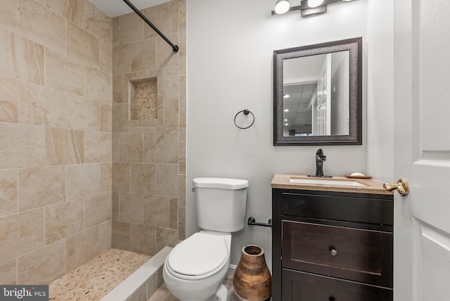 bathroom featuring a tile shower, vanity, and toilet