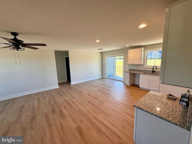 kitchen with white cabinets, light hardwood / wood-style floors, sink, and stone countertops