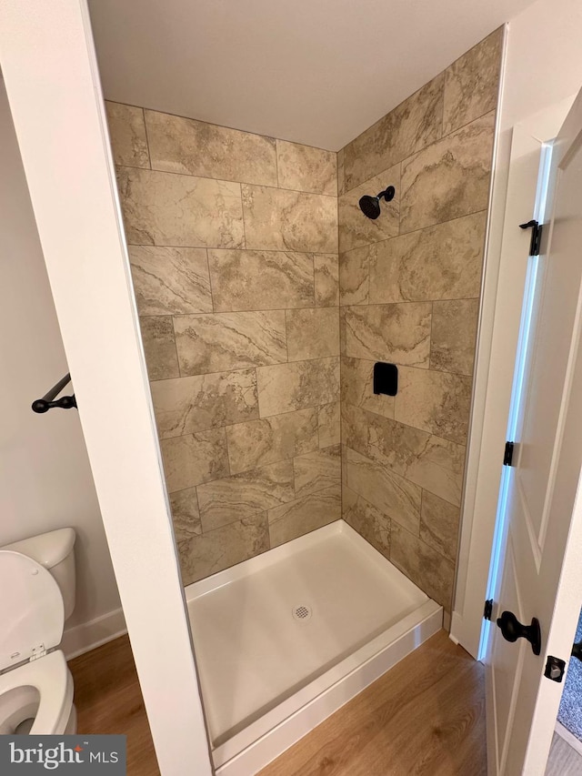 bathroom with toilet, hardwood / wood-style flooring, and tiled shower