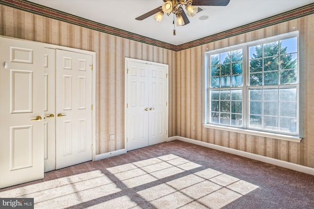 unfurnished bedroom featuring carpet, ceiling fan, and two closets