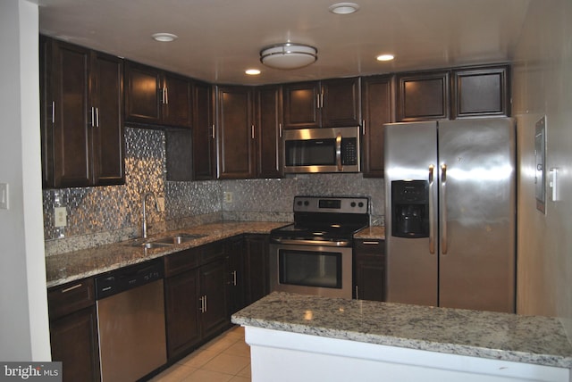 kitchen with sink, stainless steel appliances, light stone counters, backsplash, and light tile patterned floors