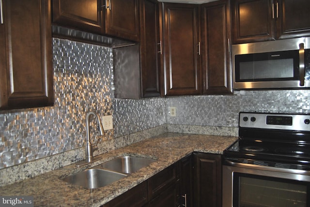 kitchen featuring sink, decorative backsplash, light stone countertops, appliances with stainless steel finishes, and dark brown cabinetry