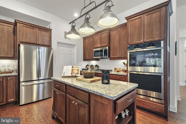 kitchen featuring stainless steel appliances, dark wood-type flooring, light stone counters, backsplash, and decorative light fixtures