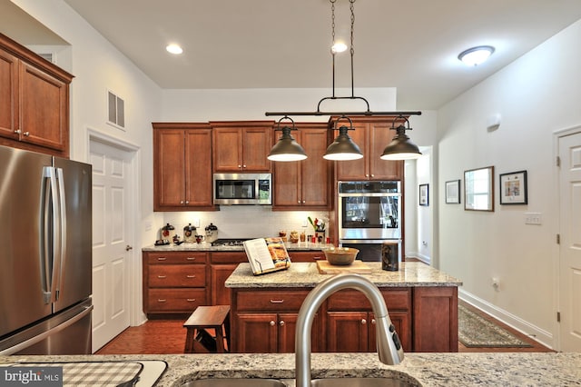 kitchen with tasteful backsplash, light stone countertops, appliances with stainless steel finishes, and hanging light fixtures