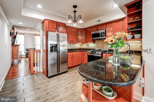 kitchen with stainless steel appliances, light hardwood / wood-style floors, dark stone counters, backsplash, and pendant lighting