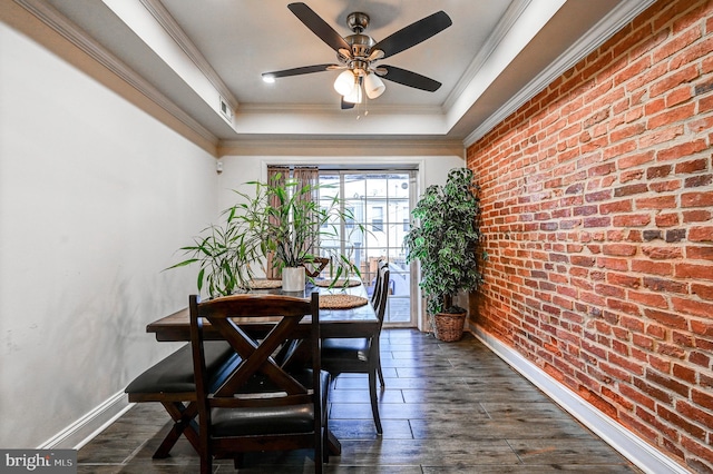 dining space with ornamental molding, a raised ceiling, dark hardwood / wood-style flooring, ceiling fan, and brick wall