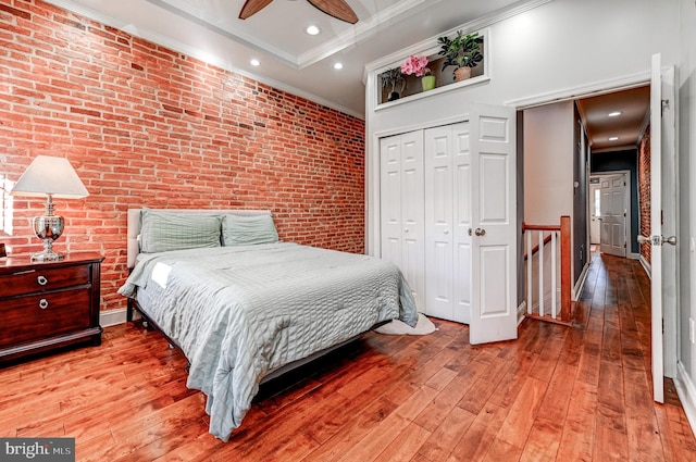 bedroom with ornamental molding, ceiling fan, a closet, light hardwood / wood-style flooring, and brick wall