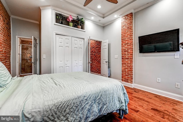 bedroom with a closet, crown molding, hardwood / wood-style floors, ceiling fan, and brick wall