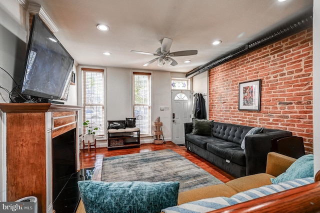 living room featuring a fireplace, dark hardwood / wood-style flooring, brick wall, and ceiling fan