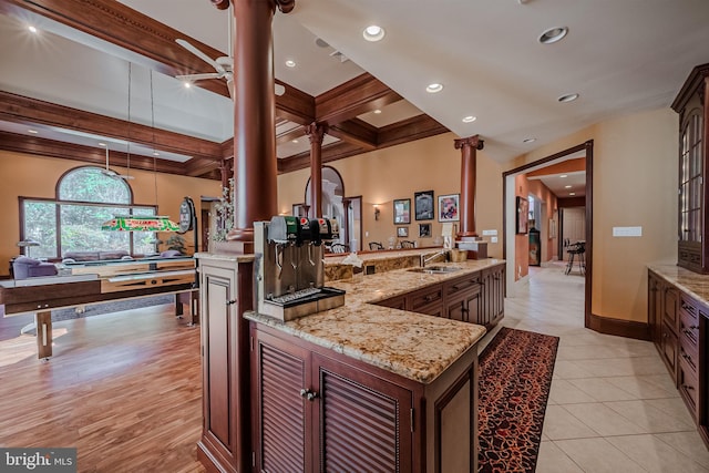 kitchen featuring light wood-type flooring, light stone counters, beamed ceiling, and a center island