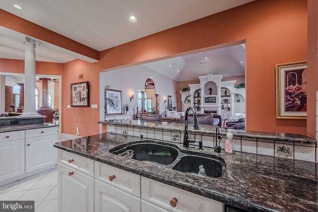 kitchen featuring white cabinets, sink, light tile patterned floors, decorative columns, and dark stone countertops