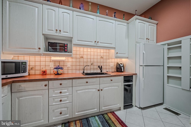 kitchen featuring white refrigerator, white cabinets, sink, tasteful backsplash, and light tile patterned floors