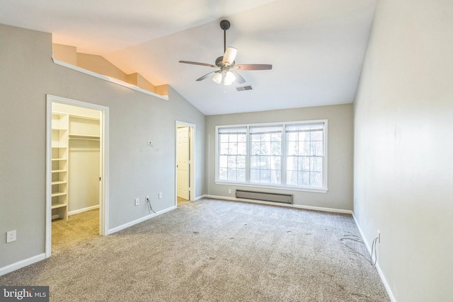 unfurnished bedroom with light carpet, ceiling fan, baseboard heating, lofted ceiling, and a walk in closet