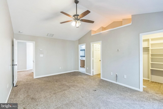 unfurnished bedroom featuring light colored carpet, a walk in closet, lofted ceiling, and ceiling fan