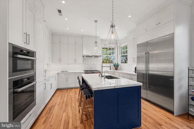 kitchen featuring white cabinets, stainless steel appliances, light hardwood / wood-style flooring, and a center island with sink