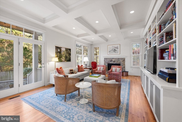 living room with a stone fireplace, coffered ceiling, a wealth of natural light, beam ceiling, and light hardwood / wood-style flooring