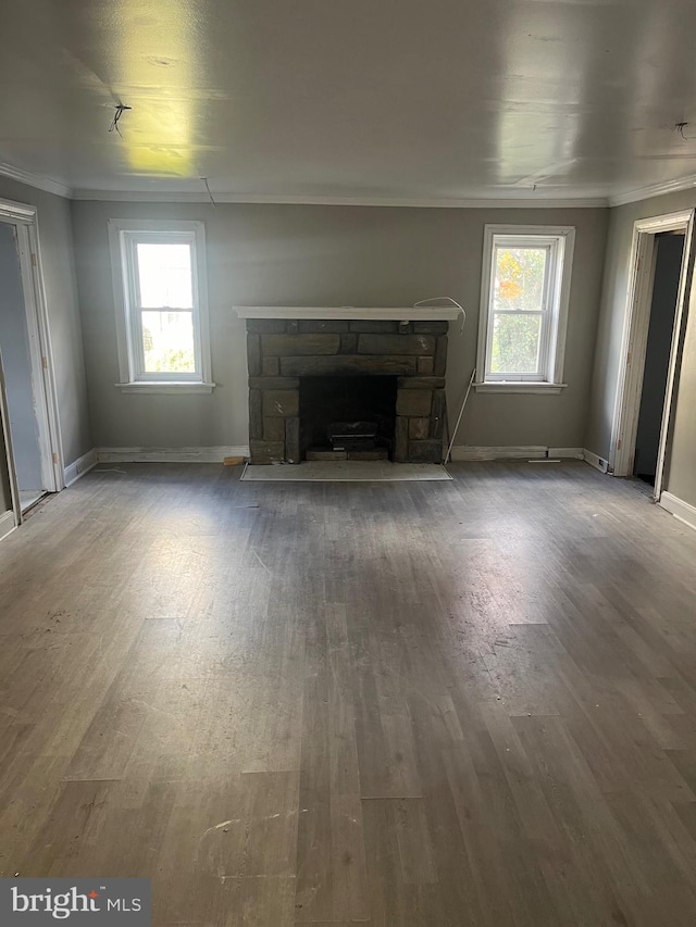 unfurnished living room featuring hardwood / wood-style flooring, a stone fireplace, plenty of natural light, and ornamental molding