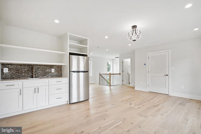 kitchen featuring light wood-type flooring, white cabinetry, backsplash, and stainless steel refrigerator