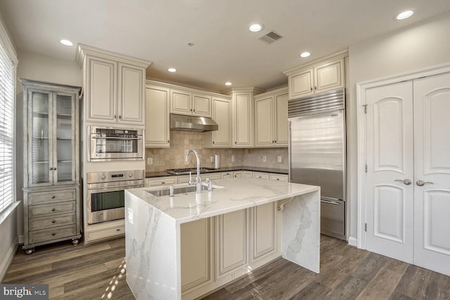 kitchen featuring dark hardwood / wood-style flooring, light stone counters, appliances with stainless steel finishes, and cream cabinets