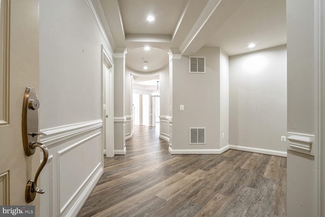 hall with wood-type flooring, ornamental molding, and a tray ceiling