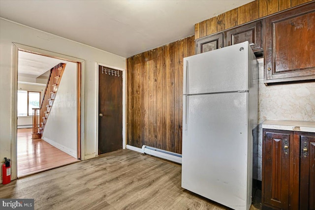 kitchen with a baseboard radiator, wood walls, white fridge, dark brown cabinets, and light wood-type flooring