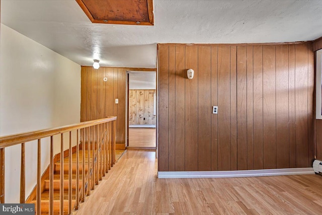 corridor featuring wood walls, light hardwood / wood-style floors, and a textured ceiling