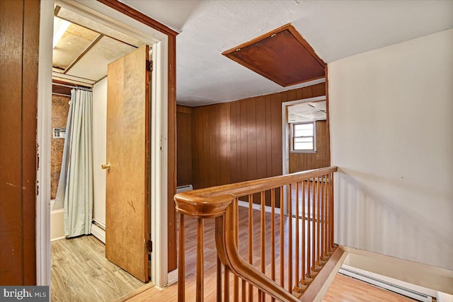 corridor featuring wooden walls, light wood-type flooring, and a baseboard heating unit