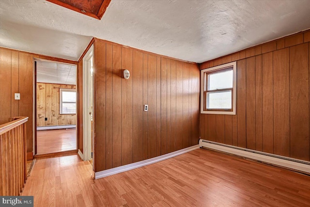 unfurnished room with a baseboard radiator, light hardwood / wood-style floors, wood walls, and a textured ceiling