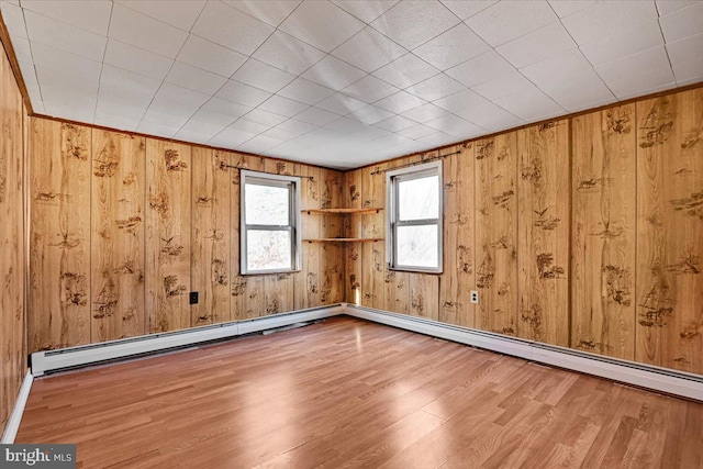 spare room featuring baseboard heating, hardwood / wood-style floors, and wood walls