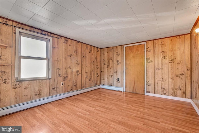 spare room featuring a baseboard radiator, wooden walls, and light hardwood / wood-style flooring