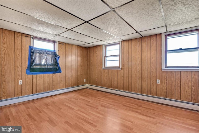 basement featuring wood walls, light wood-type flooring, and a drop ceiling