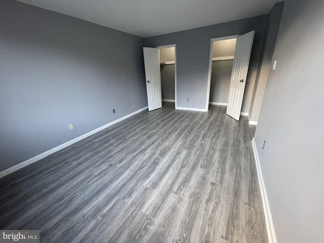 unfurnished bedroom with a walk in closet, a closet, and dark wood-type flooring