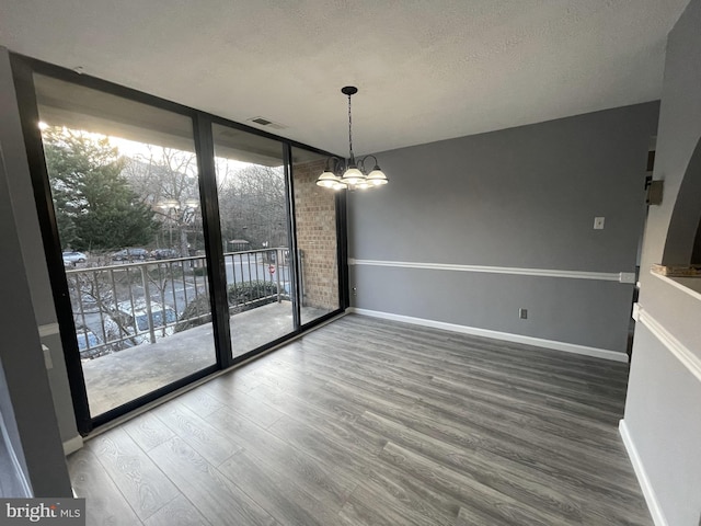 unfurnished dining area with a chandelier, hardwood / wood-style floors, a textured ceiling, and expansive windows