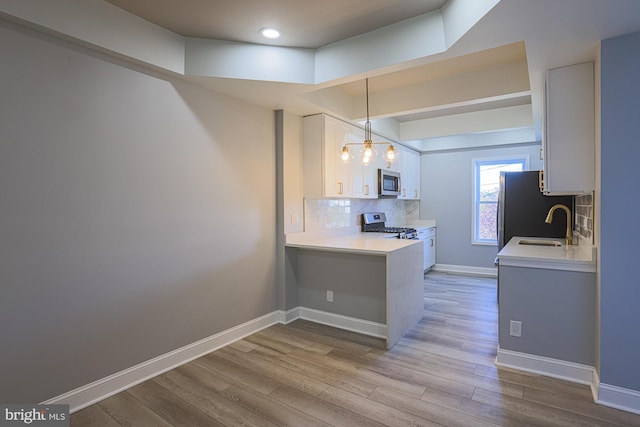 kitchen featuring backsplash, kitchen peninsula, light wood-type flooring, appliances with stainless steel finishes, and white cabinetry