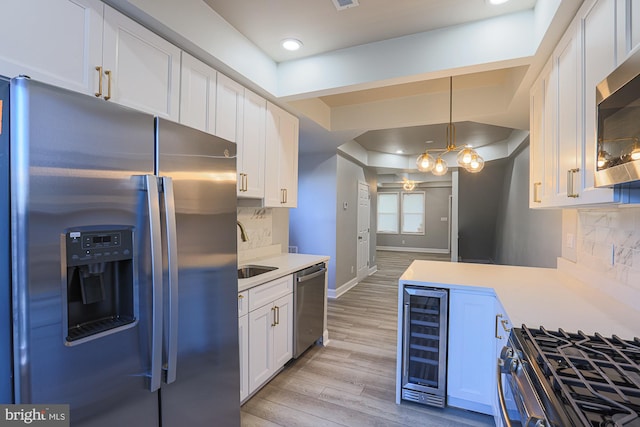 kitchen featuring backsplash, wine cooler, light hardwood / wood-style floors, white cabinetry, and stainless steel appliances