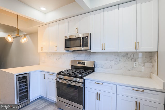 kitchen with beverage cooler, light hardwood / wood-style flooring, decorative light fixtures, white cabinets, and appliances with stainless steel finishes