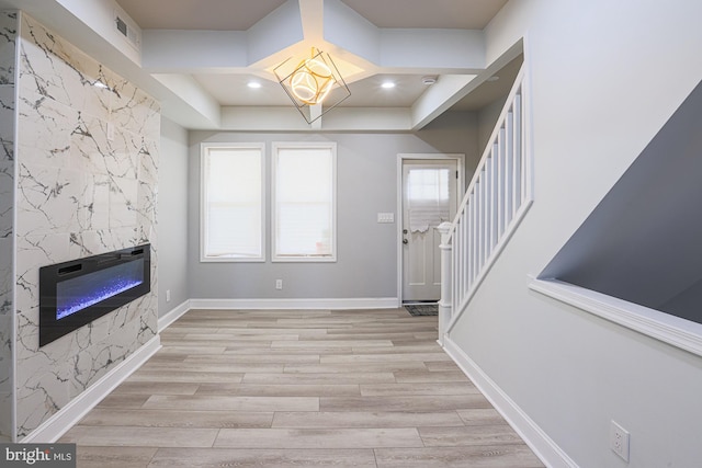 entryway with a high end fireplace, light hardwood / wood-style floors, and a notable chandelier